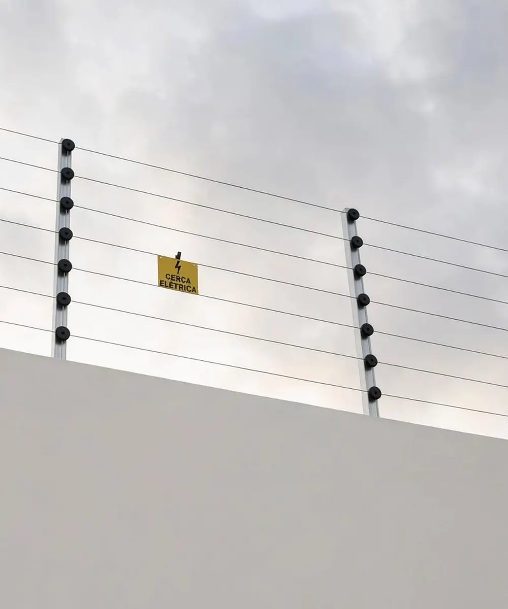 Cerca elétrica no alto de um muro, com placa de aviso